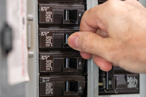 Man flipping circuit breaker. PC Electric serving Portland OR and Beaverton OR answers the common question, "Why does my circuit breaker keep tripping?"